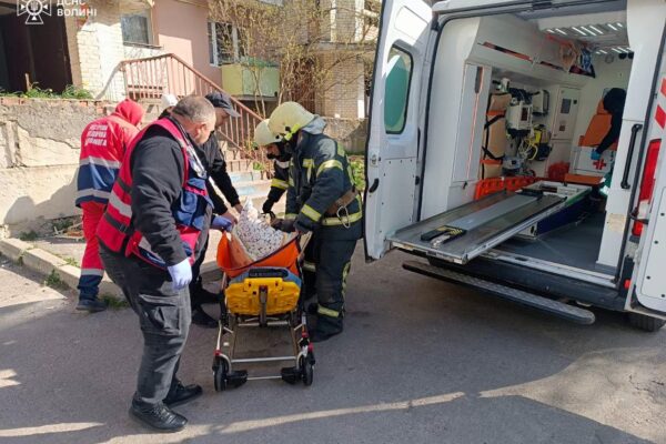 рятувальники виносять жінку, яка сама не може рухатися, до машини швидкої допомоги