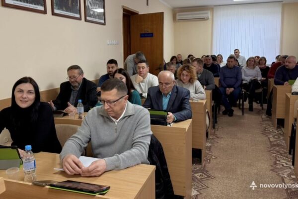 Депутати та засіданні Нововолинської міської ради під час чергової сесії: у залі повністю зайняті ряди, присутні працюють із планшетами та документами.