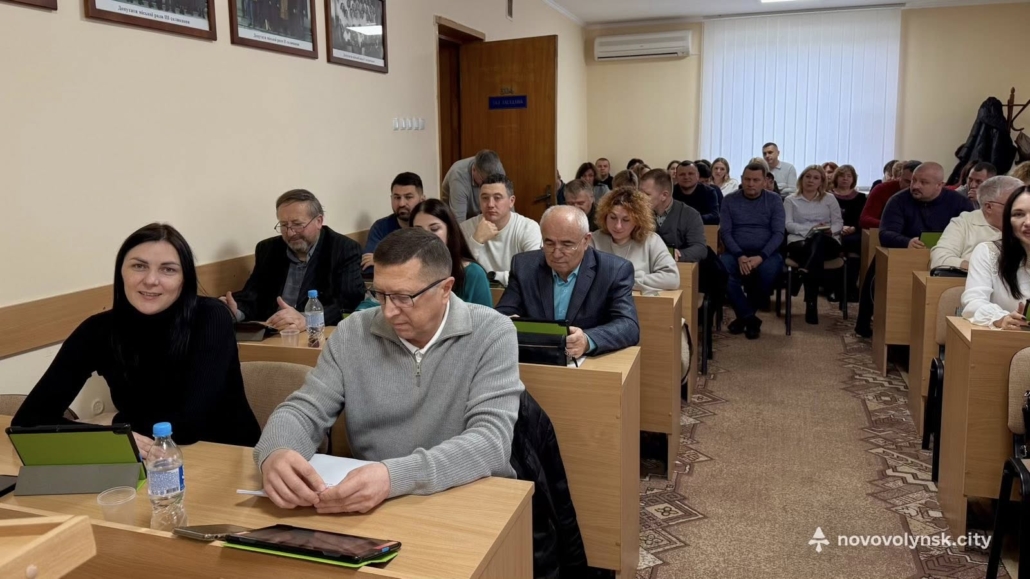 Депутати та засіданні Нововолинської міської ради під час чергової сесії: у залі повністю зайняті ряди, присутні працюють із планшетами та документами.